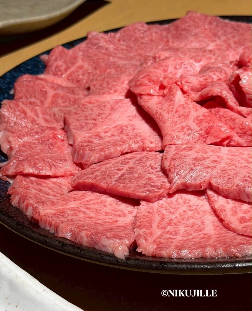 Close-up of thinly sliced raw wagyu arranged on a black plate, showing delicate marbling and a glossy finish.