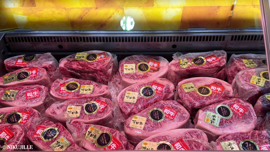 Rows of Japanese A5 Wagyu beef cuts with marbling, each individually wrapped and labeled with authenticity tags in a retail meat display case
