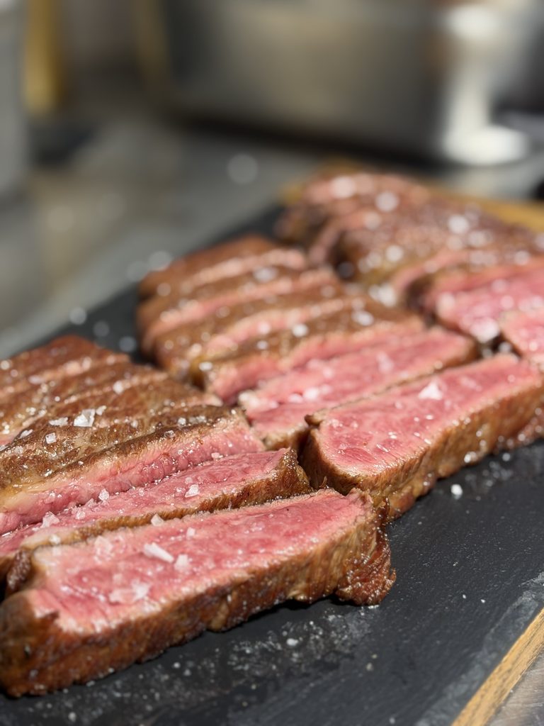 Close-up of sliced grilled wagyu steak on a slate board, seared brown on the outside and pink inside, topped with flaky sea salt.