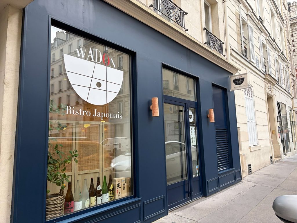 Navy blue storefront of Wadon, a Japanese bistro in Paris, with a white logo on the window and sake bottles displayed inside.