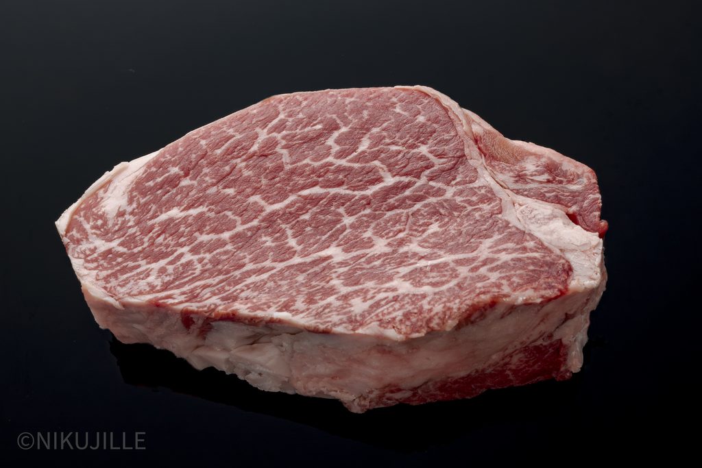 A thick raw slice of Japanese wagyu tenderloin on a black surface, showing fine, delicate marbling across the tender red face.